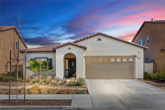 mediterranean / spanish-style house with an attached garage, a tiled roof, concrete driveway, and stucco siding