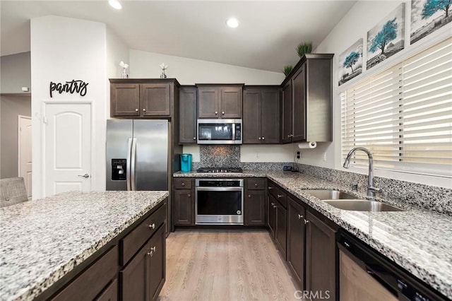 kitchen with stainless steel appliances, light wood-style floors, vaulted ceiling, a sink, and light stone countertops