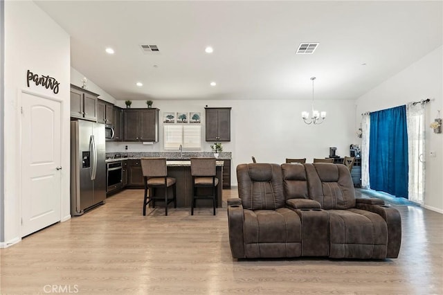 living room featuring lofted ceiling, light wood-type flooring, visible vents, and a notable chandelier