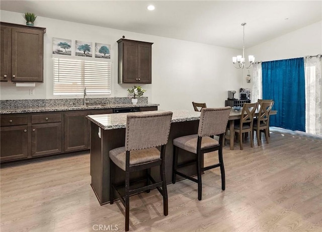 kitchen with dark brown cabinetry, light stone countertops, a chandelier, and a center island