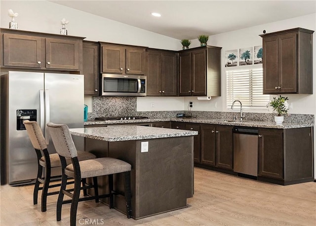 kitchen featuring stainless steel appliances, a kitchen island, light stone countertops, light wood-type flooring, and a kitchen breakfast bar