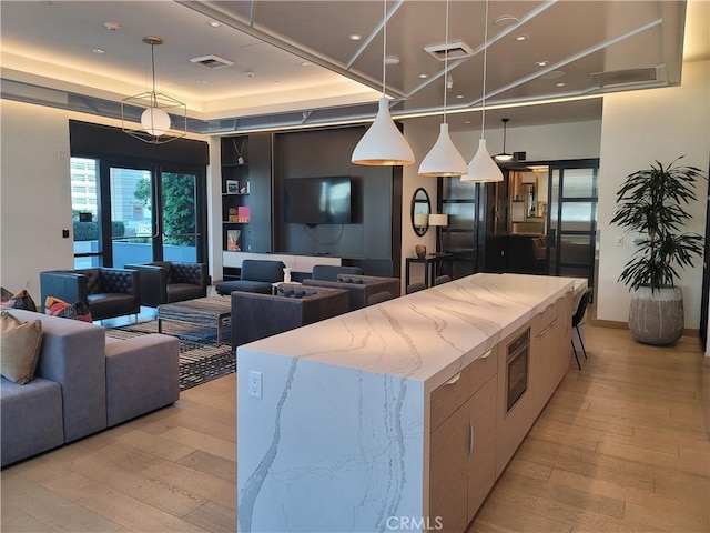 kitchen featuring open floor plan, visible vents, a raised ceiling, and light wood finished floors