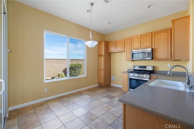 kitchen featuring stainless steel appliances, dark countertops, hanging light fixtures, light brown cabinetry, and a sink