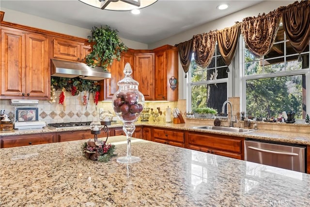 kitchen featuring decorative backsplash, appliances with stainless steel finishes, light stone countertops, range hood, and a sink