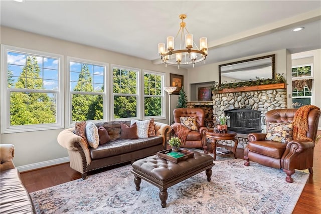 living room with a chandelier, a stone fireplace, baseboards, and wood finished floors