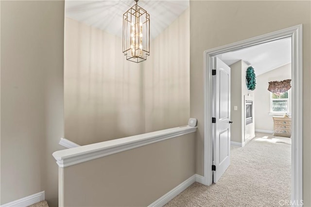 hallway featuring carpet, a notable chandelier, and baseboards