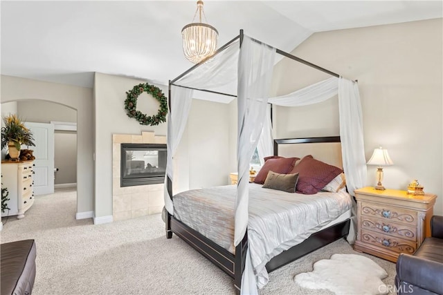 bedroom featuring arched walkways, a fireplace, a notable chandelier, carpet flooring, and vaulted ceiling