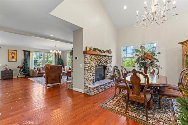 dining space with baseboards, wood finished floors, a high ceiling, a fireplace, and a chandelier