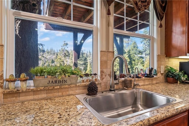 kitchen featuring tasteful backsplash, brown cabinetry, a sink, and light stone countertops