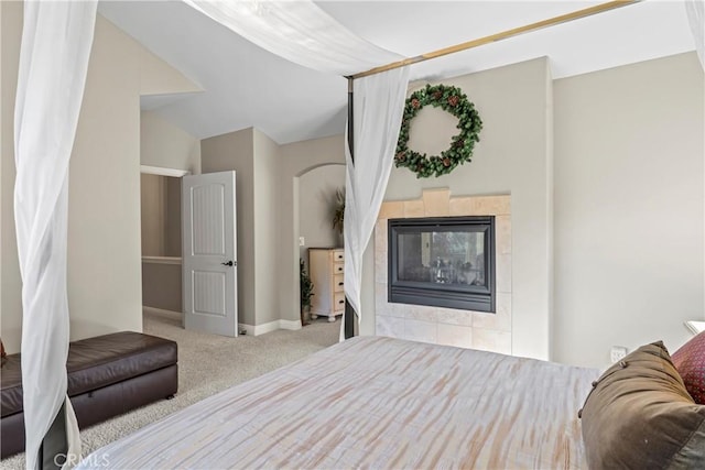 bedroom featuring a tile fireplace, light carpet, vaulted ceiling, and baseboards