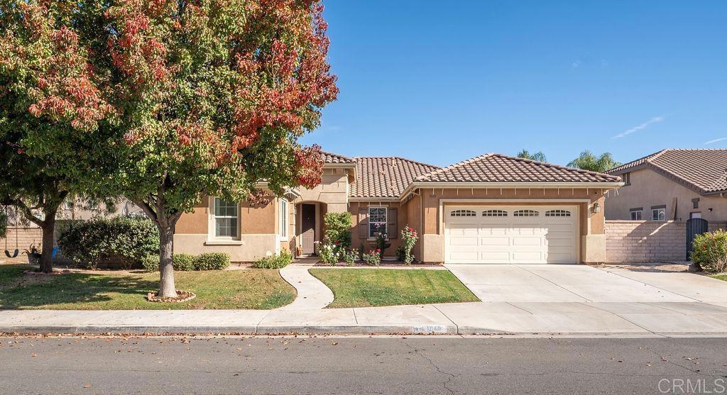 view of front of house featuring an attached garage, a tiled roof, driveway, stucco siding, and a front lawn