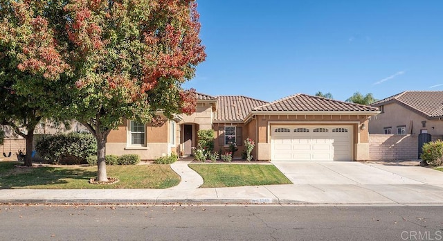 view of front of house featuring an attached garage, a tiled roof, driveway, stucco siding, and a front lawn