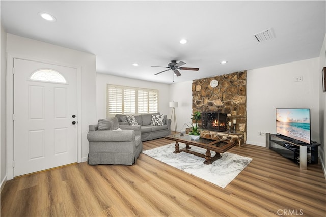 living room with recessed lighting, visible vents, a stone fireplace, and wood finished floors