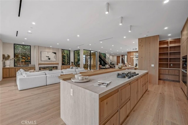 kitchen with a fireplace, open floor plan, light countertops, a center island, and light wood finished floors