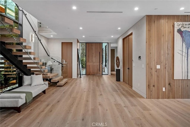 foyer with wooden walls, light wood-type flooring, stairway, and recessed lighting