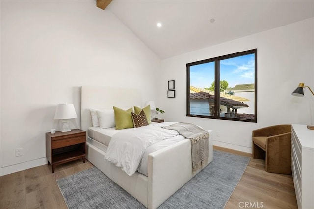 bedroom featuring baseboards, beamed ceiling, and light wood finished floors