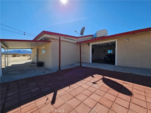 rear view of property with driveway, an attached carport, a patio, and stucco siding