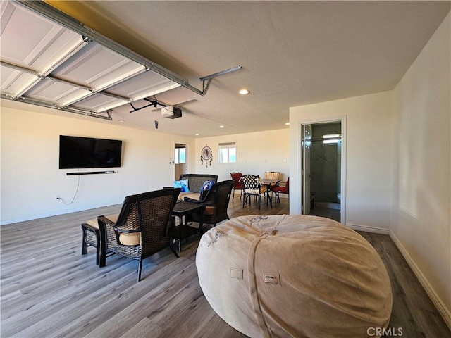 living area featuring a garage, baseboards, wood finished floors, and recessed lighting