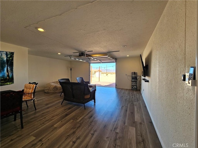 living room with a garage, dark wood-style flooring, a textured ceiling, and baseboards