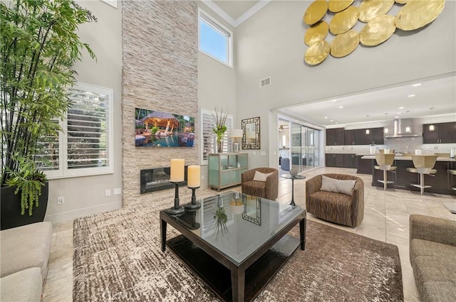 living area featuring light tile patterned floors, baseboards, visible vents, crown molding, and a stone fireplace