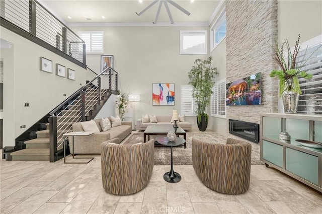 living area featuring stairs, a fireplace, a high ceiling, and crown molding