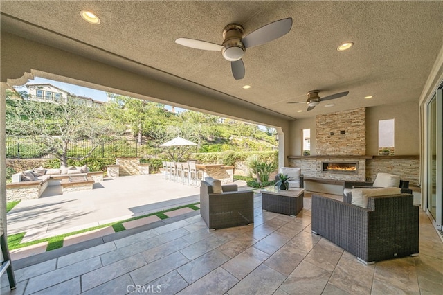 view of patio / terrace featuring an outdoor living space with a fireplace, fence, and a ceiling fan