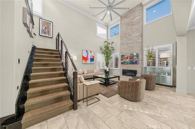 living room with a towering ceiling, stairs, a fireplace, and crown molding