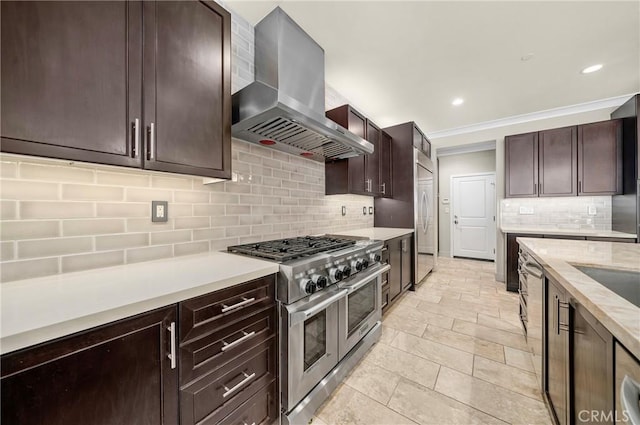 kitchen with high quality appliances, light countertops, dark brown cabinets, wall chimney exhaust hood, and tasteful backsplash