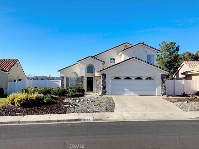 mediterranean / spanish-style home featuring stucco siding, an attached garage, fence, stone siding, and driveway