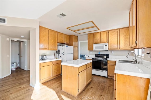 kitchen featuring light wood-style flooring, white appliances, a kitchen island, a sink, and visible vents