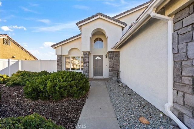 doorway to property with stone siding, fence, and stucco siding