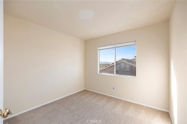 spare room featuring light colored carpet and baseboards