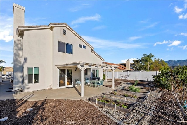 rear view of house featuring stucco siding, a patio area, fence, a pergola, and a garden