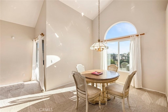 dining space with light carpet, an inviting chandelier, baseboards, and high vaulted ceiling