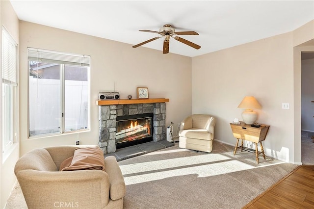 living area featuring a ceiling fan, a fireplace, baseboards, and wood finished floors