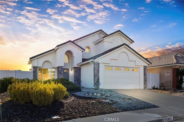 view of front facade featuring driveway, stone siding, an attached garage, fence, and stucco siding