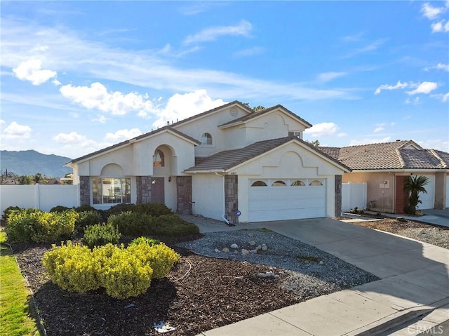 mediterranean / spanish-style house featuring a tile roof, concrete driveway, fence, a garage, and stone siding