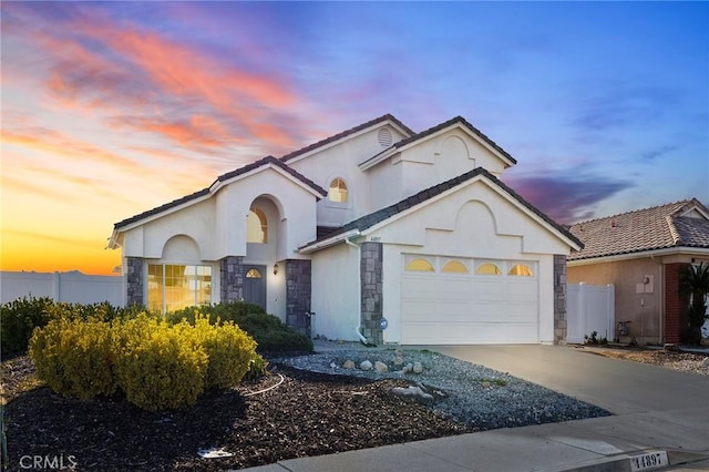 view of front facade with a garage, concrete driveway, stone siding, fence, and stucco siding