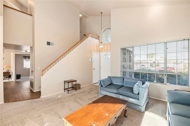 carpeted living area featuring stairway, a towering ceiling, visible vents, and baseboards