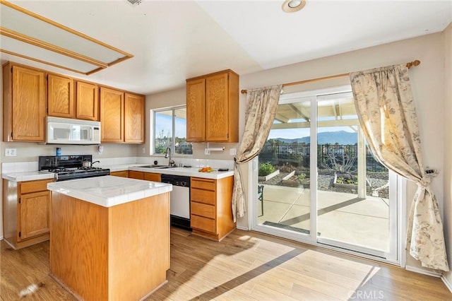 kitchen with light wood finished floors, stainless steel dishwasher, white microwave, a sink, and black gas stove