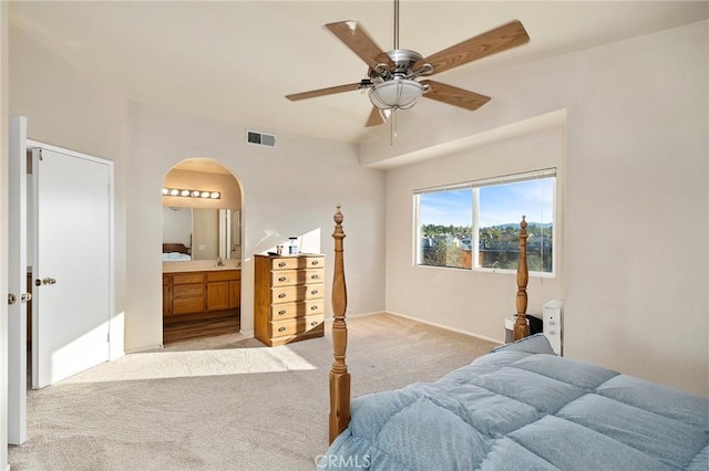 bedroom featuring visible vents, arched walkways, a ceiling fan, light colored carpet, and ensuite bathroom