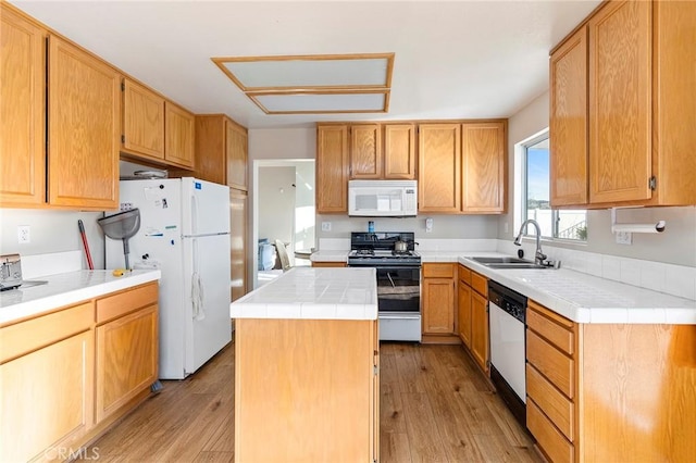 kitchen with white appliances, a kitchen island, light wood finished floors, and a sink