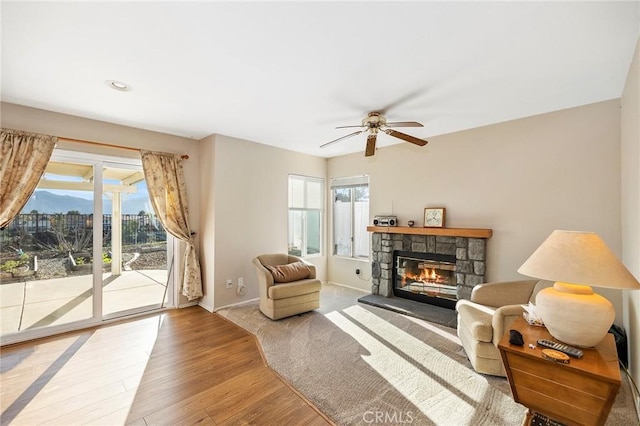 sitting room featuring a stone fireplace, wood finished floors, a ceiling fan, and baseboards