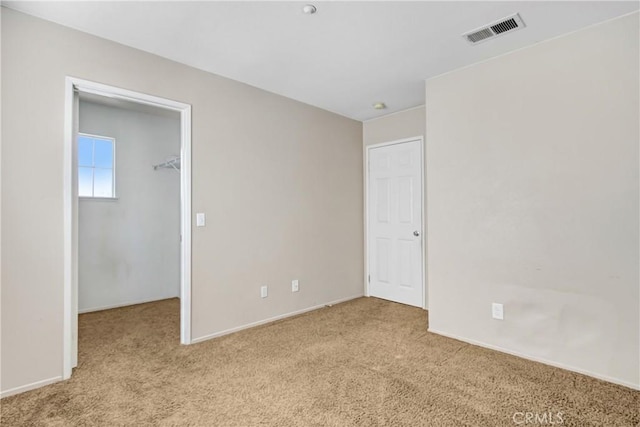 unfurnished bedroom featuring a walk in closet, a closet, visible vents, and carpet