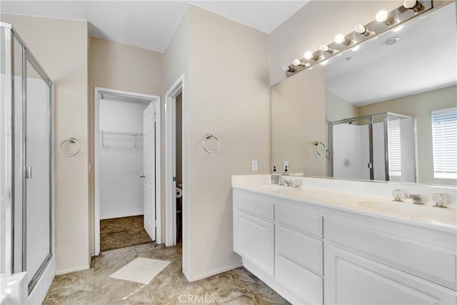 bathroom featuring a walk in closet, double vanity, a stall shower, a sink, and baseboards