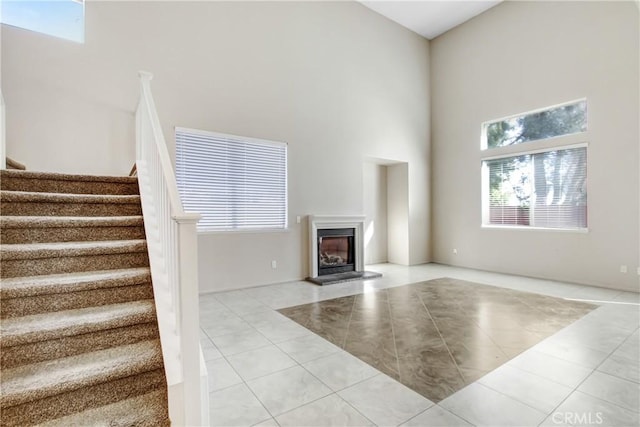 unfurnished living room featuring a glass covered fireplace, tile patterned flooring, stairway, and a high ceiling