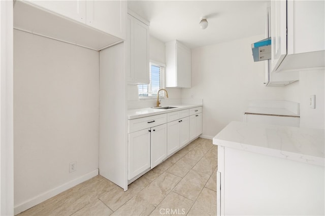 kitchen with light stone countertops, baseboards, white cabinetry, and a sink