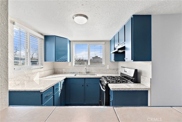 kitchen featuring stainless steel range with gas cooktop, a healthy amount of sunlight, a sink, blue cabinets, and under cabinet range hood