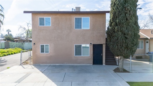 back of house with stucco siding, a gate, a patio area, fence, and stairs