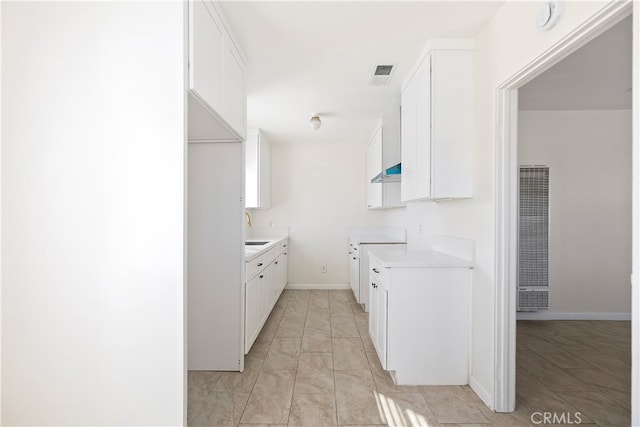 kitchen featuring wall chimney range hood, white cabinetry, visible vents, and a sink